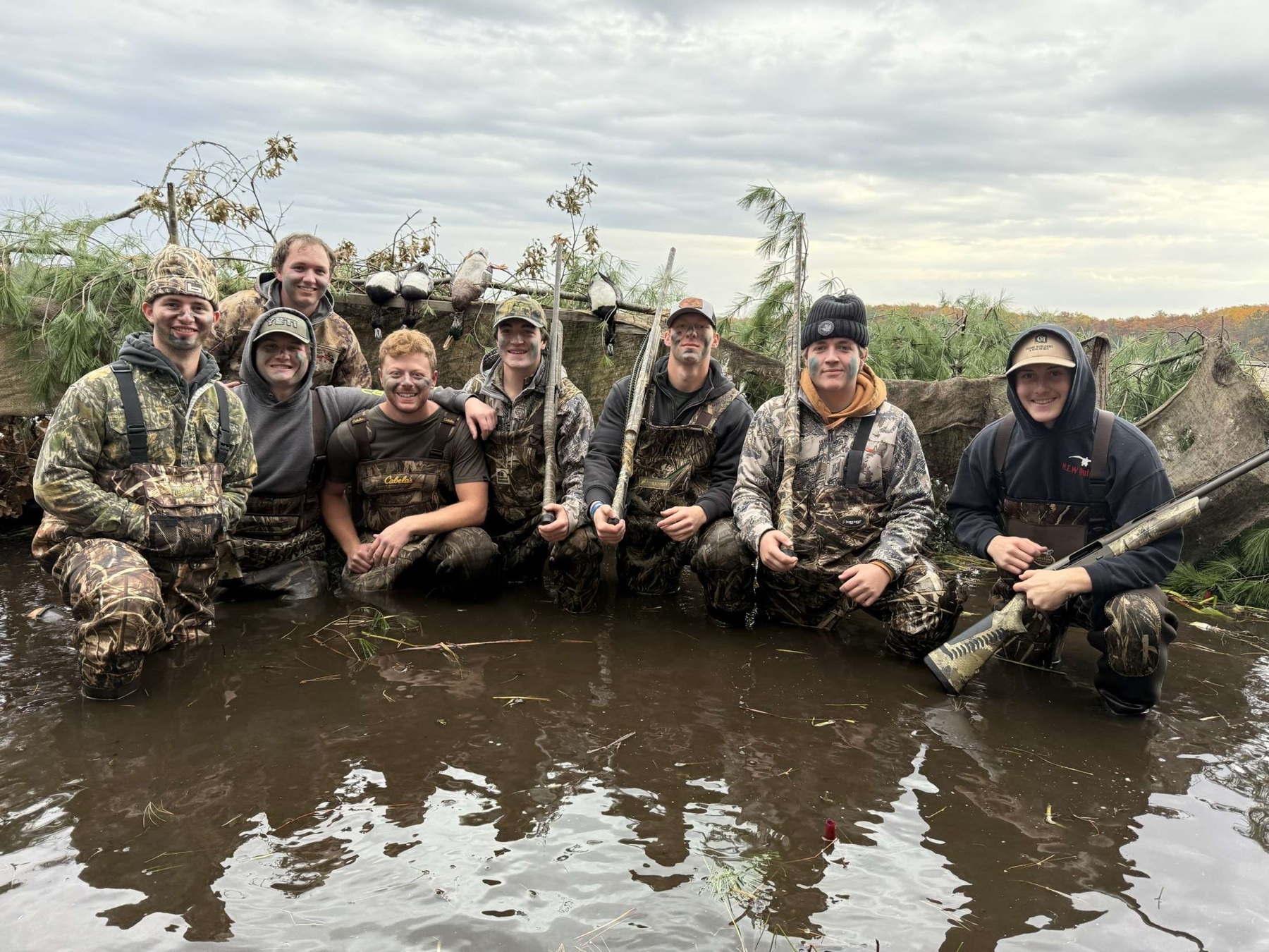 A group of duck hunters posing together in a brush-lined blind