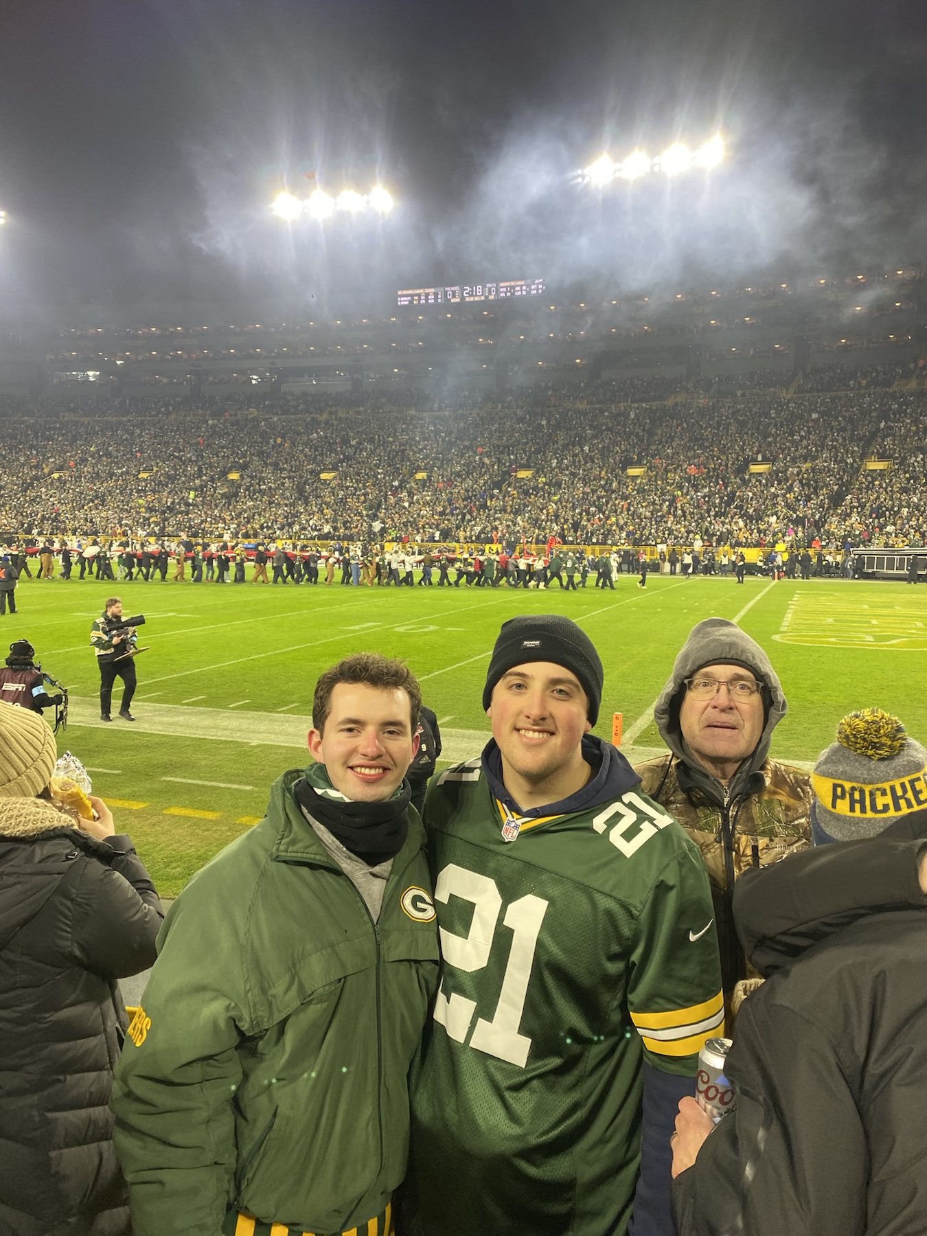 A group in Packers clothing beside a football field under stadium lights