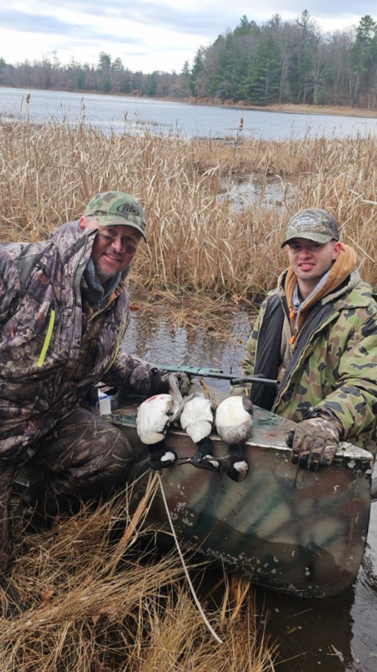 Two duck hunters beside a small boat in a reedy wetland